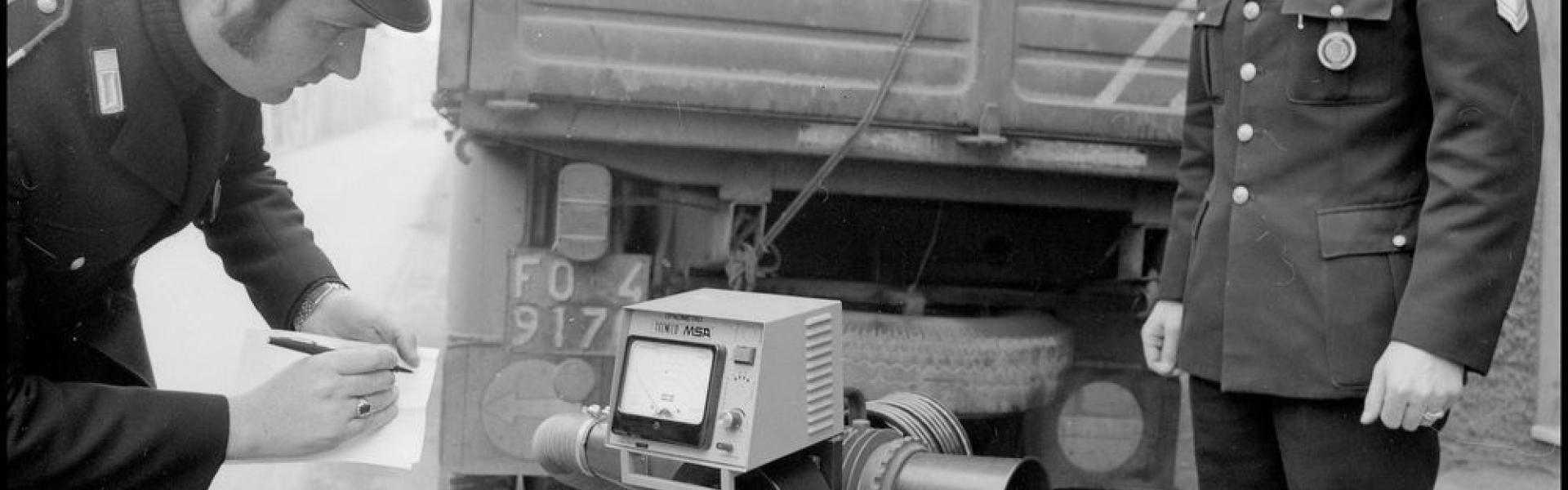 immagine di due Vigili Urbani intenti a rilevare le misure e ad annotarle di gas di scarico di un camion con l'opacimetro ( 1975 ).  