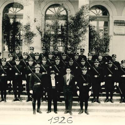 Immagine d'epoca del 1926 del Corpo dei Vigili Urbani di Rimini schierata sulle scale davanti ad una palazzina della zona mare. Sullo sfondo le arcate del palazzo e le porte finestre per accedervi   