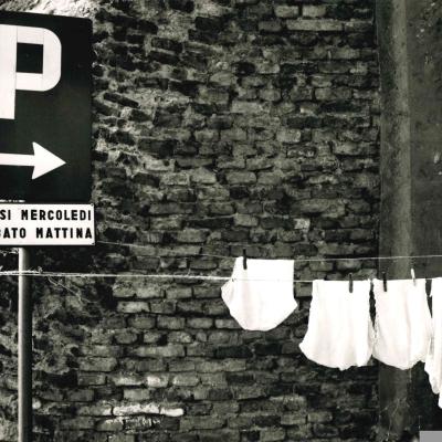 cartello stradale indicante il parcheggio in piazza Malatesta con appeso un filo per stendere i panni con mutande e altra biancheria intima sullo sfondo le mura malatestiane