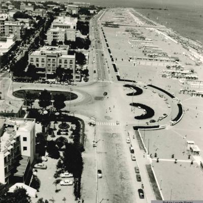 foto aerea di piazza Tripoli in direzione del porto canale, con la spiaggia e gli edifici con sullo sfondo il Nettuno e il torrente Ausa. 