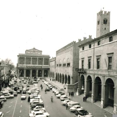 foto aerea di piazza Cavour con sullo sfondo il teatro Galli con striscioni pubblicitari appesi, il palazzo dell'Arengo, del Podestà e la vecchia Pescheria quando era ancora possibile parcheggiare