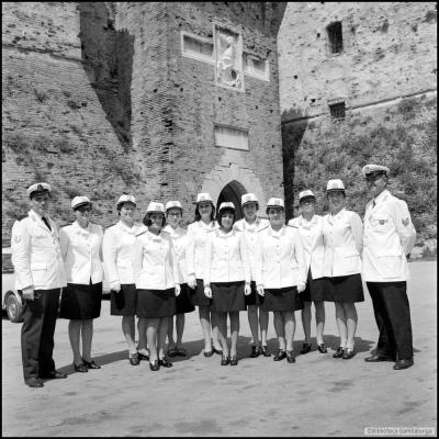 immagine delle prime donne assunte nei Vigili Urbani di Rimini il primo giugno 1964. Ai lati del gruppo di neoassunte vi sono due sottufficiali. Sullo sfondo l'ingresso a Castel Sigismondo