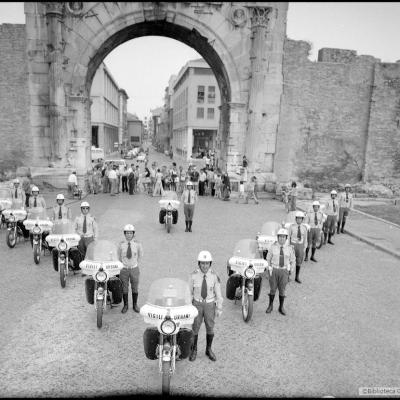 Immagine dei motociclisti dei Vigili Urbani di Rimini posizionati a triangolo davanti all'Arco d'Augusto. Sullo sfondo largo Giulio Cesare e il Corso d'Augusto