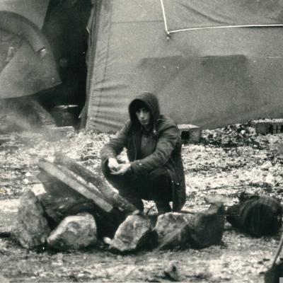 immagine di una ragazzo all'interno della tendopoli di Laviano creata dopo il terremoto del 1980 che, accovacciato, cerca di scaldarsi con un fuoco improvvisato tra le tende