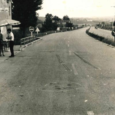 immagine della strada Consolare di San Marino all'altezza della Trattoria del Coniglio ( 1966  ). Sull'asfalto i segni di una frenata di un'auto. A lato nei pressi della trattoria ci sono due donne e un uomo intenti a parlare  