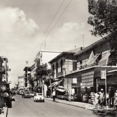 metà anni '60. Panoramica di viale Dati a Viserba con i negozi a lato della carreggiata. A lato della strada un Vigile Urbano controlla il traffico veicolare e pedonale  